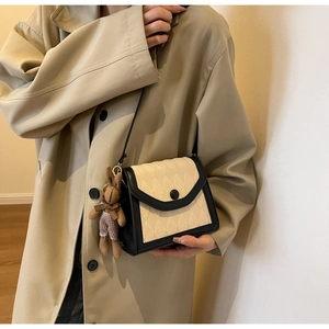 Détail d'un sac bandoulière matelassé crème avec bordure noire et breloque lapin en peluche
