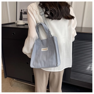 Detailed back view of a light gray canvas crossbody bag worn in a modern room