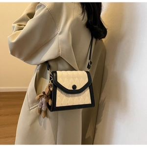 Détail du sac bandoulière avec texture matelassée beige, cuir noir et pendentif ours