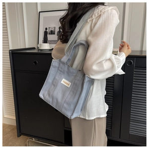 Detail of light blue canvas tote bag with FASHION label and adjustable shoulder strap