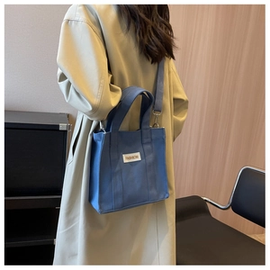 Detail of dark blue canvas crossbody bag with Fashion label worn over a beige coat