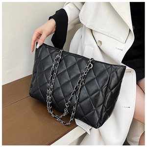 Detail of black quilted tote bag with silver chain strap on a model in white coat