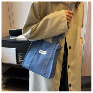 Blue canvas tote bag with FASHION patch shown on a shoulder strap in a lifestyle setting