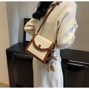Sac bandoulière matelassé beige avec charme en peluche porté par un mannequin élégant