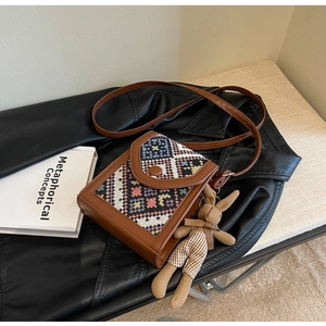 Detail of a brown ethnic style crossbody bag with woven patterns and a bunny doll charm