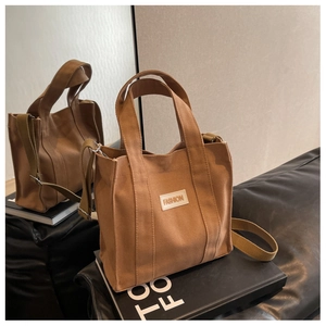 Detail of brown canvas tote bag with FASHION patch and adjustable shoulder strap