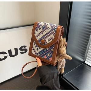 Detail of woven flap crossbody bag featuring a cute rabbit doll charm and metal buckle