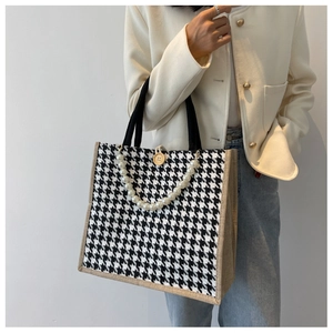 Detail of houndstooth tote bag featuring pearl chain strap and wooden button closure