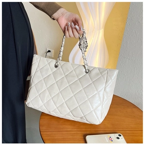Detail of white quilted leather tote bag with silver chain strap held by a model