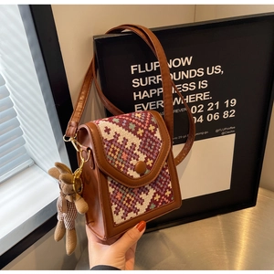 Close-up of brown leather crossbody bag with geometric woven flap and cute bear pendant