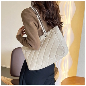 Close-up of white quilted tote bag featuring silver chain strap worn by a model