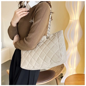 Chic quilted tote bag in beige with chain strap held by model in a warm interior