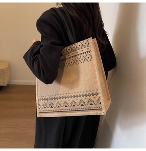 Linen tote bag with black geometric patterns and woven handles shown on a model