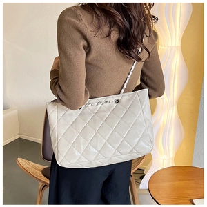 Detail of a large beige quilted tote bag with chain strap worn over the shoulder