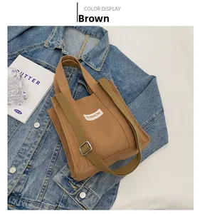 Detail of brown canvas handbag with 'FASHION' label, adjustable strap on denim background