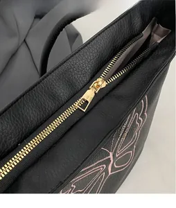 Close-up of litchi textured black tote bag featuring pink butterfly embroidery and gold zipper