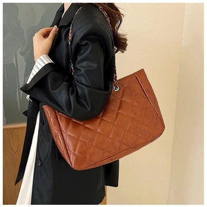 Detail view of large brown quilted tote bag with silver chain strap worn by a model