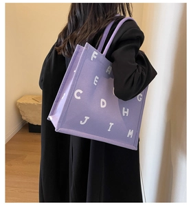 Side view of a purple large capacity canvas tote bag with white letter print on a model