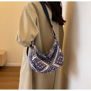 Detailed view of bohemian geometric woven half-moon bag worn with a beige trench coat