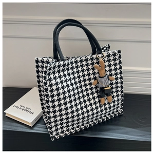 Detail of houndstooth tote bag with a black rope handle and a cute bunny plush charm