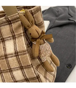 Close-up of a brown knitted rabbit charm with a bow on a stylish wool shoulder bag
