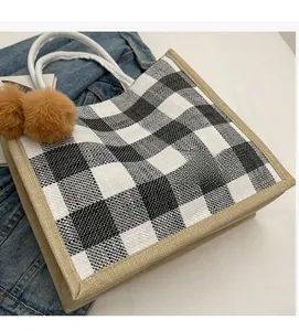 Detail of waffle plaid tote bag featuring brown pom-pom charms and woven rope handles