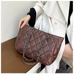 Dark brown quilted tote bag with silver chain strap shown on a model against a white wall