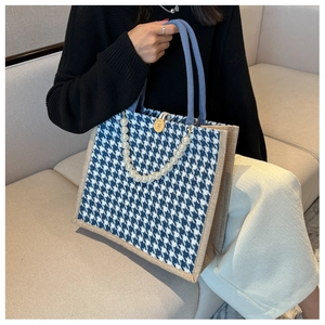 Close-up of blue houndstooth tote bag with white pearl strap and vintage button detail