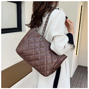 Detailed view of brown quilted tote bag with chain strap worn by a model in casual setting