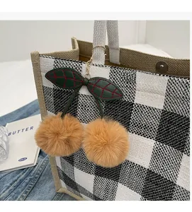 Detail of plush cherry bag charm with brown fur pom-poms on a checkered tote bag