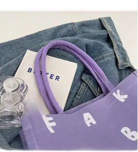 Detailed macro view of purple canvas tote bag with woven handles and white lettering