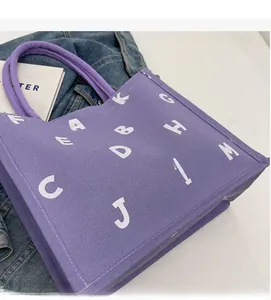 Close-up of purple canvas tote bag with white lettering and reinforced handle detail