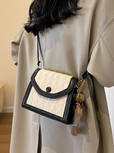 Petit sac bandoulière matelassé beige et noir avec breloque ours sur un trench-coat kaki