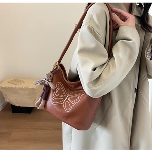 Detail of caramel brown tote bag featuring white butterfly embroidery and a bunny charm