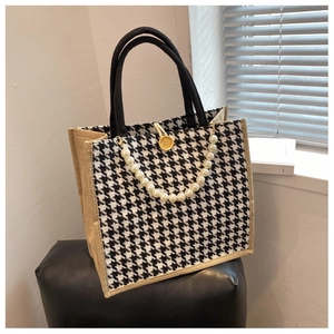 Detail of houndstooth tote bag featuring pearl chain strap and yellow button accent