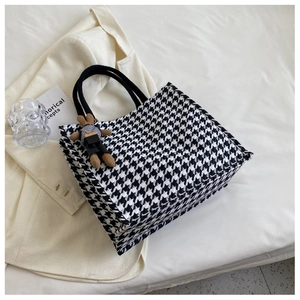 Detail shot of a houndstooth tote bag with a brown bunny charm on an ivory suit jacket