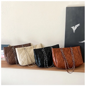 Detailed view of quilted chain tote bags in brown, beige, and black on a wooden table