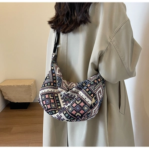 Detailed side view of ethnic woven saddle bag with geometric patterns on a beige trench coat