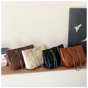 Quilted tote bags in four colors with chain straps displayed on a wooden shelf