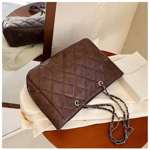 Detailed view of dark brown quilted tote bag with metallic chain straps on wooden surface