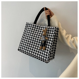 Detail of black and white houndstooth tote bag with brown bunny plush charm accessory