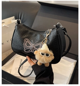 Détail du sac en cuir grainé noir avec broderie papillon rose et breloque peluche