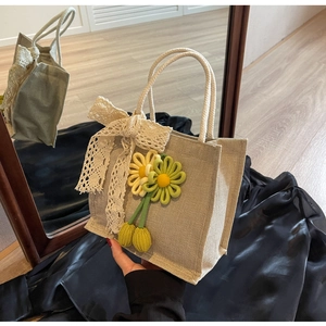 Detail of beige linen handbag featuring large lace bow and crochet flower accents