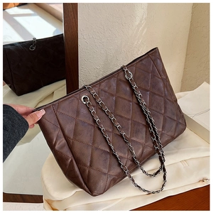 Detail view of the brown quilted leather texture and silver chain strap on this tote bag
