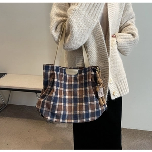 Detail view of large plaid wool tote bag with a plush rabbit charm for winter commute