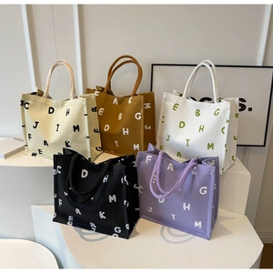 Group display of five large canvas tote bags with letter prints on white steps