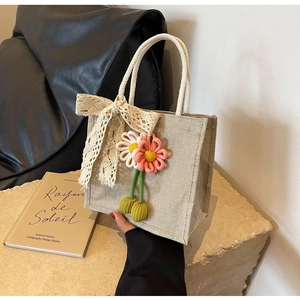 Detail of beige jute lunch bag featuring large lace bow and handmade woven flower charms