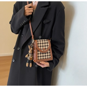 Detail of retro checkerboard crossbody bag with leather trim and rabbit charm accessory