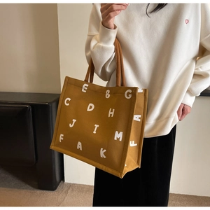 Close-up of a mustard yellow canvas tote bag with white letter print and large capacity