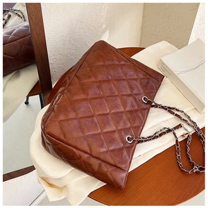 Detailed view of large quilted brown tote bag with silver chain straps on a wooden table